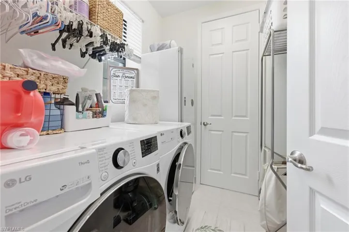 Dedicated laundry area featuring a white LG ThinQ washer, overhead shelving, white paneled doors, and light-toned flooring