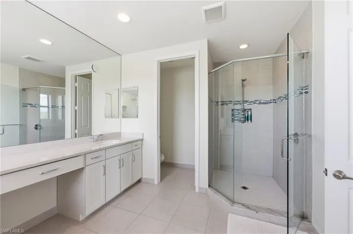 Spacious bathroom featuring a glass-enclosed walk-in shower with decorative tile accent, a long vanity with dual sinks, ample under-cabinet storage, and recessed lighting