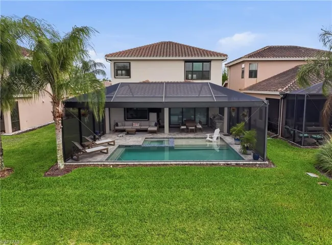 Rear exterior featuring a screened-in pool and spa, covered patio, and manicured lawn
