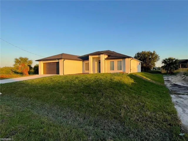 Prairie-style home featuring a front lawn, driveway, a garage, and stucco siding