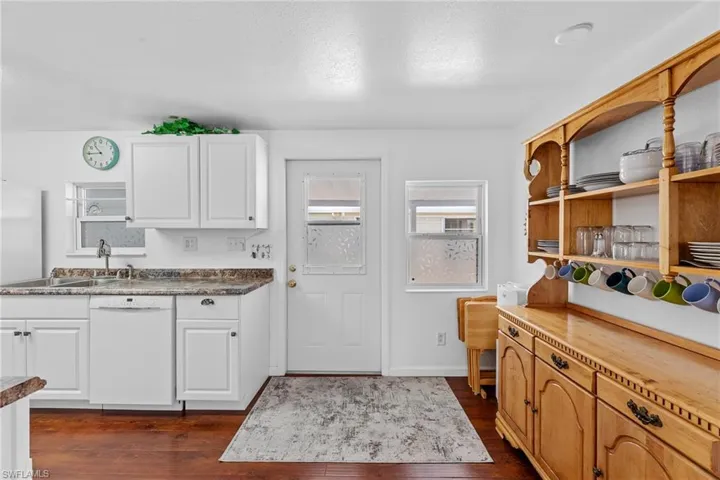 Kitchen featuring dark wood-type flooring, a textured ceiling, white dishwasher, and white cabinetry
