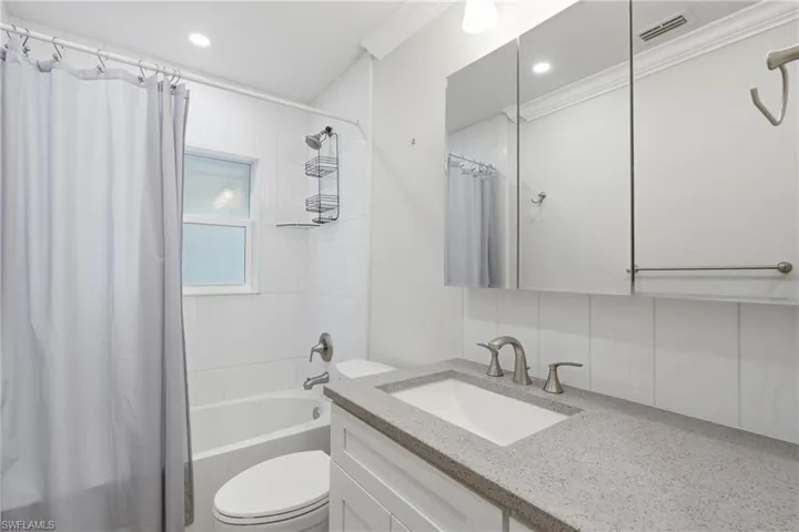 Full bathroom featuring a white vanity cabinet with a speckled countertop, an undermount sink, and brushed nickel fixtures