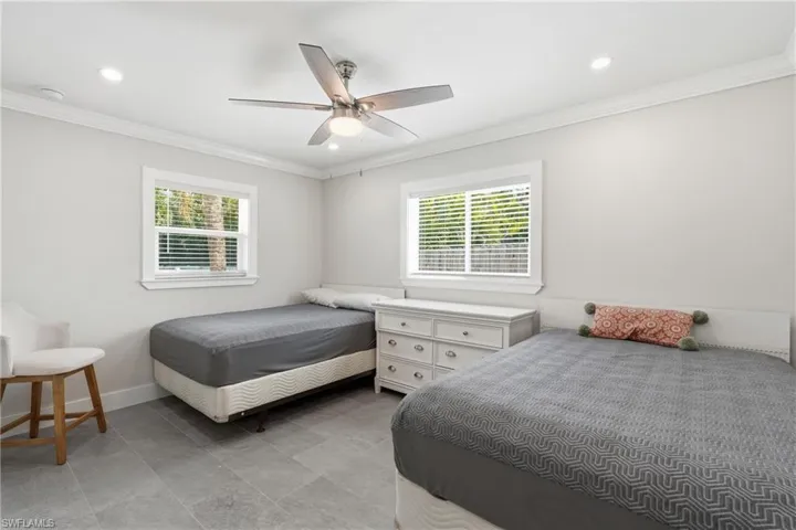 Modern bedroom featuring light gray walls, gray tile flooring, and white crown molding