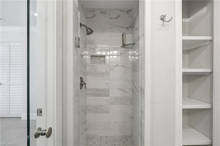 Walk-in shower featuring marble-patterned tile walls, a built-in shower niche, and a mosaic tile floor