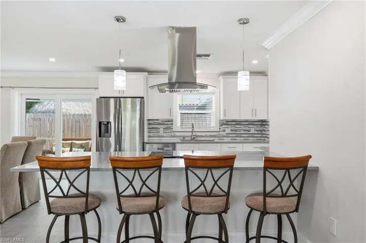 Contemporary kitchen featuring a large island with a light-toned quartz countertop, stainless steel appliances, white cabinetry, and a textured tile backsplash