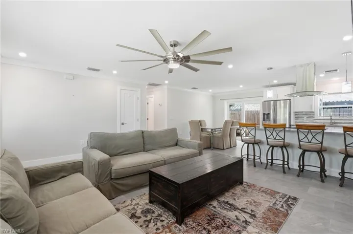 Open-concept living space featuring a modern ceiling fan, recessed lighting, crown molding, and wood-finish tile flooring