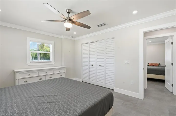Interior room featuring light gray walls, crown molding, a window with horizontal blinds, wood-finish ceiling fan, and louvered bi-fold closet doors