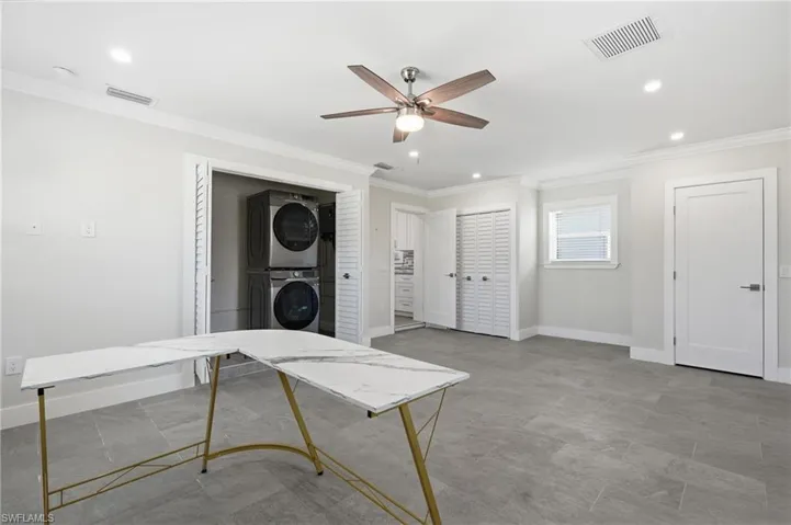 Spacious room featuring gray plank tile flooring, recessed lighting, a ceiling fan with wood-finish blades, and a dedicated laundry closet with stacked appliances.
