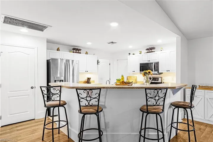 Kitchen with a kitchen breakfast bar, light wood-style flooring, white cabinets, recessed lighting, and a kitchen island with sink
