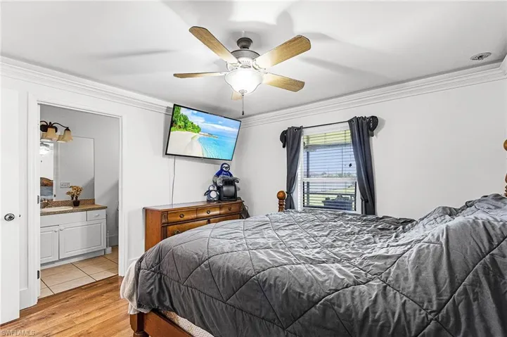 Bedroom with ornamental molding, wood finished floors, a ceiling fan, and connected bathroom