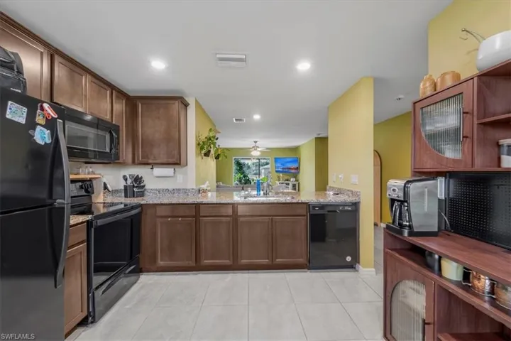 Kitchen featuring dark wood cabinetry, speckled stone countertops, ceramic tile flooring, and black appliance suite