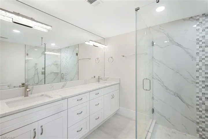 Full bath with a sink, visible vents, a marble finish shower, and double vanity