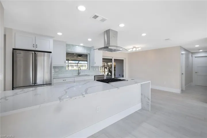 Kitchen featuring tasteful backsplash, island range hood, white cabinets, stainless steel appliances, and a sink