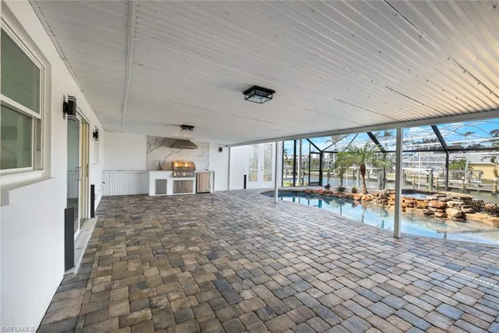 View of patio with area for grilling, a grill, glass enclosure, an outdoor pool, and french doors