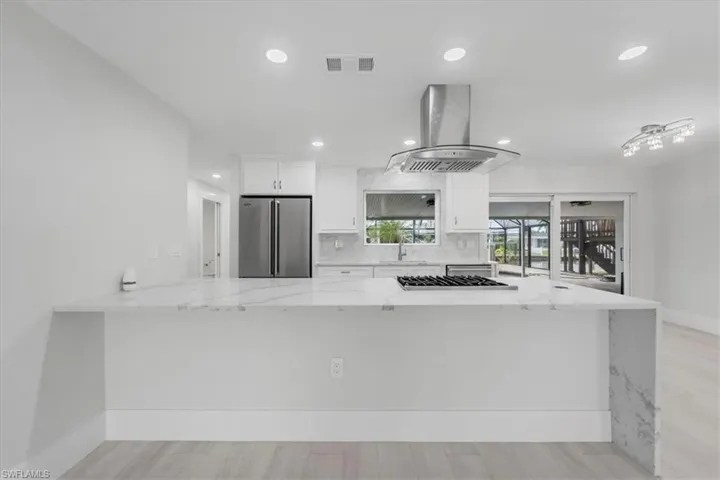 Kitchen featuring light stone counters, white cabinets, a peninsula, appliances with stainless steel finishes, and recessed lighting