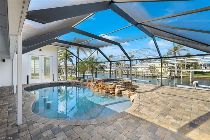 Outdoor pool featuring a water view, a patio, french doors, and a lanai