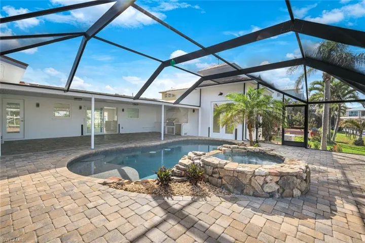 Pool with an in ground hot tub, a patio, and glass enclosure