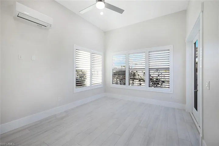 Empty room featuring light wood-type flooring, a wall mounted air conditioner, baseboards, and a ceiling fan