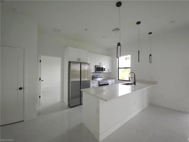 Kitchen with stainless steel appliances, light tile flooring, pendant lighting, sink, and white cabinetry