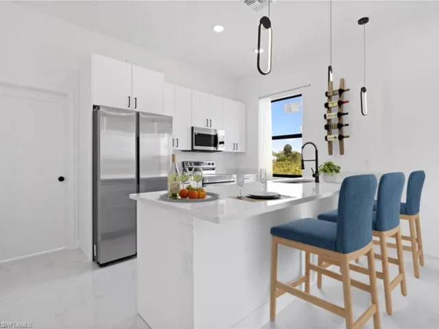 Kitchen featuring stainless steel appliances, a kitchen breakfast bar, a kitchen island with sink, white cabinetry, and pendant lighting