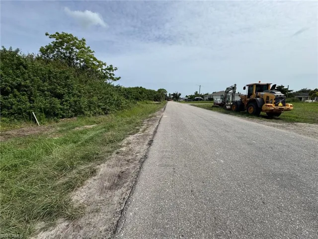 Roadside property featuring a paved road, undeveloped land with natural vegetation, and distant residential structures