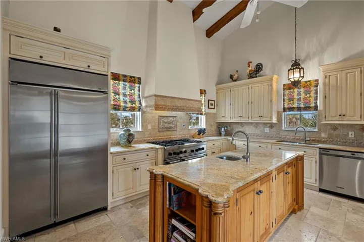 Kitchen featuring premium appliances, light stone counters, cream cabinetry, high vaulted ceiling, and beamed ceiling