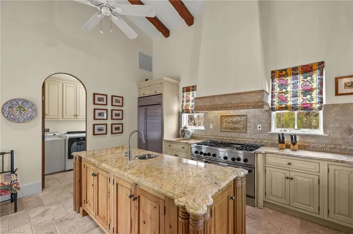 Kitchen with cream cabinetry, high vaulted ceiling, premium appliances, light stone countertops, and custom exhaust hood