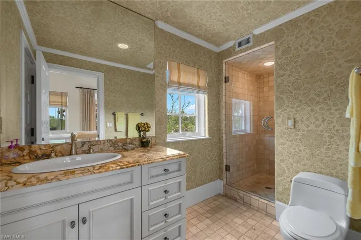 Bathroom featuring wallpapered walls, ornamental molding, a shower stall, vanity, and light tile patterned floors