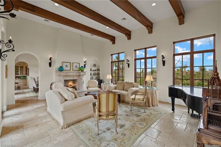 Living room with beam ceiling, stone tile flooring, a high end fireplace, arched walkways, and a towering ceiling