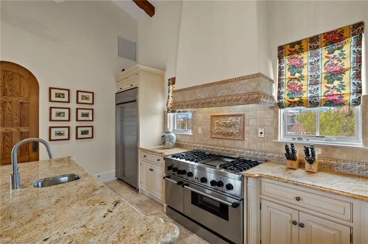 Kitchen with cream cabinets, premium appliances, light stone counters, custom range hood, and a high ceiling