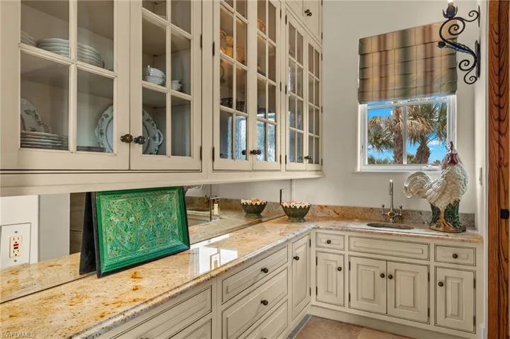 Bar area featuring cream cabinets, light stone countertops, and glass insert cabinets