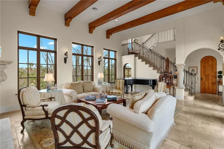 Living room with arched walkways, stairs, beamed ceiling, a towering ceiling, and stone tile floors