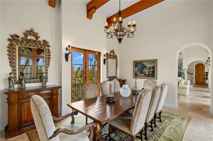 Dining space featuring arched walkways, a towering ceiling, french doors, beamed ceiling, and stone tile flooring