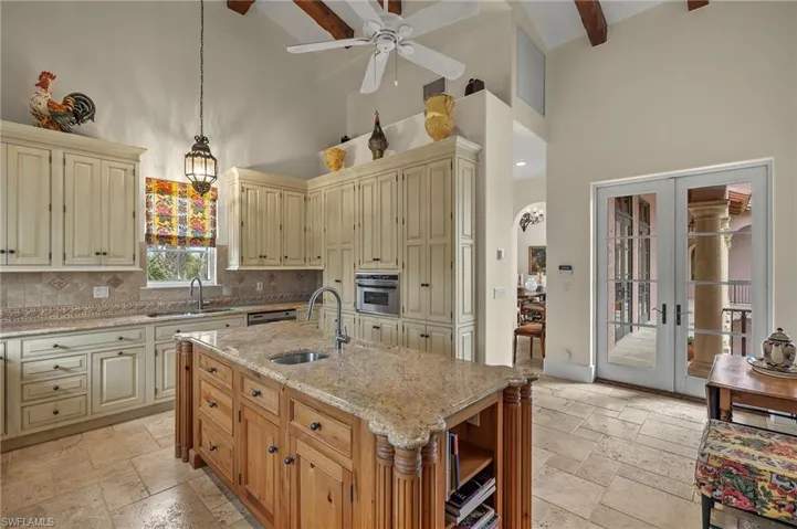 Kitchen featuring cream cabinetry, stone tile floors, a towering ceiling, decorative light fixtures, and light stone countertops