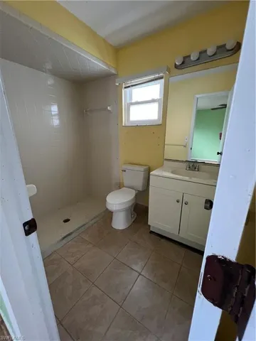 Bathroom with a tile shower, tile patterned flooring, vanity, and toilet