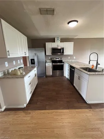 Kitchen featuring hardwood / wood-style floors, white cabinetry, appliances with stainless steel finishes, and sink