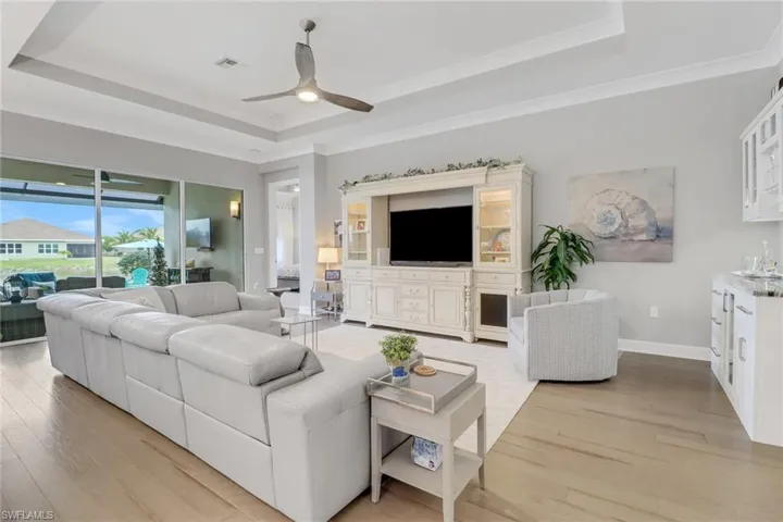 Living room with ceiling fan, light wood-type flooring, a tray ceiling, and ornamental molding