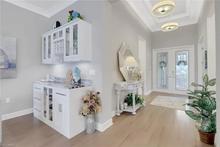 Entrance foyer with ornamental molding, light wood-type flooring, a raised ceiling, and french doors