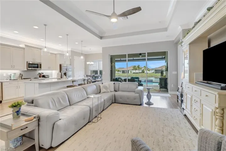 Living room featuring ceiling fan with notable chandelier, light wood-type flooring, and a tray ceiling