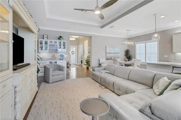Living room with ceiling fan with notable chandelier, a raised ceiling, ornamental molding, and light hardwood / wood-style floors
