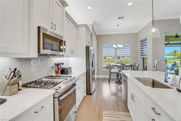 Kitchen with light stone countertops, decorative light fixtures, white cabinets, appliances with stainless steel finishes, and sink