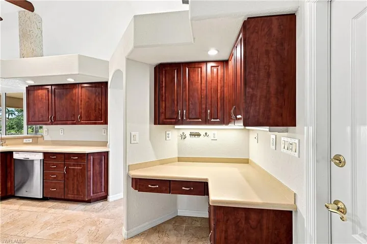 Elegant kitchen workspace featuring rich cherry wood cabinetry, cream-colored countertops, stainless steel appliances, recessed lighting, and a generous built-in desk area with additional storage drawers