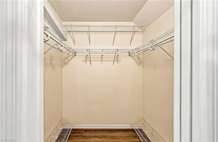 Walk-in closet featuring full wire shelving, hanging rods, wood-finish flooring, and light neutral wall tones