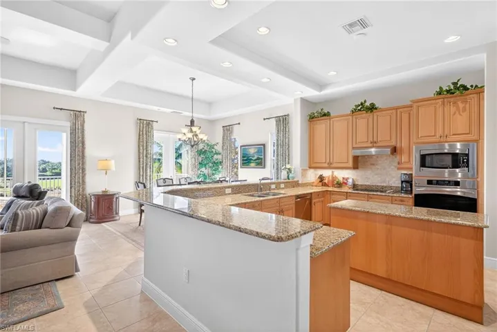 Kitchen featuring a peninsula, a chandelier, backsplash, light stone counters, and decorative light fixtures
