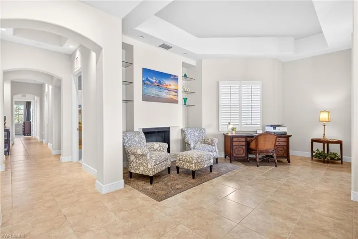 Sitting room with arched walkways, a tray ceiling, a desk, a fireplace, and light tile patterned floors