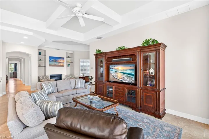 Living area with arched walkways, light tile patterned floors, beam ceiling, ceiling fan, and coffered ceiling