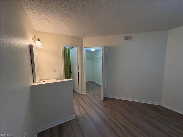 Unfurnished bedroom with a walk in closet, a textured ceiling, and dark wood finished floors