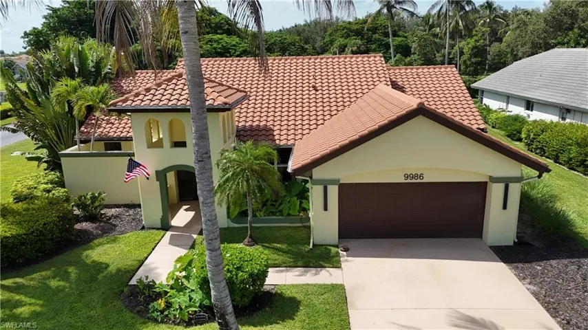 Spanish-style architecture featuring a tile roof, stucco exterior, attached garage, concrete driveway, and mature landscaping