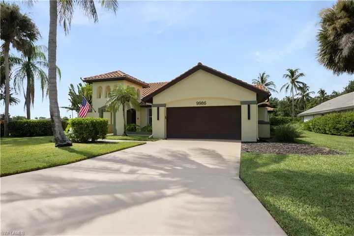 Mediterranean-style exterior with a tile roof, arched architectural details, mature landscaping, and an attached two-car garage