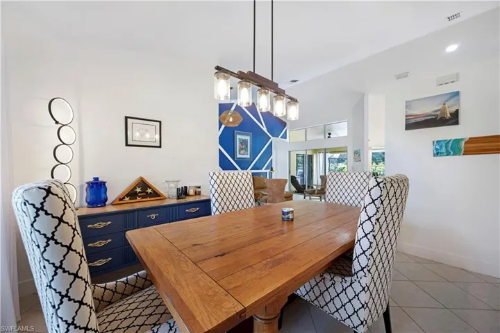 Vaulted ceilings, a linear pendant light fixture, a built-in sideboard with gold-finish hardware, and a wood-finish dining table